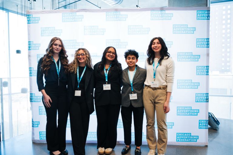 Group of people wearing conference credentials stand in front of a photo backdrop.