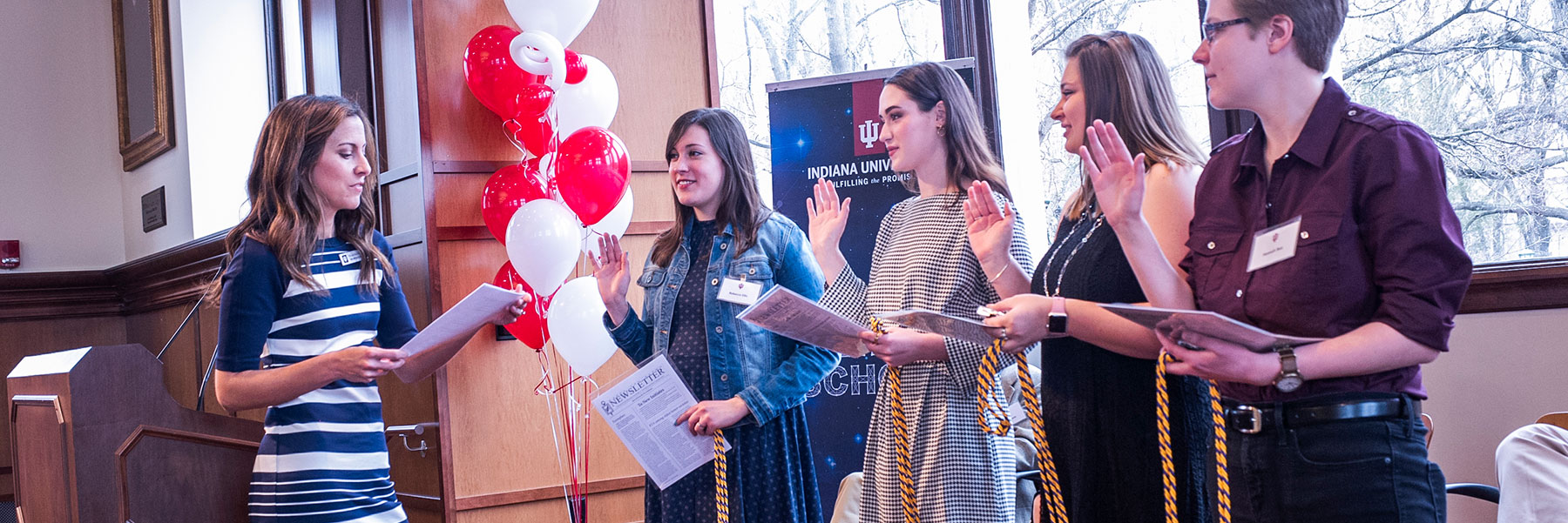 Four students hold up their right hands as Nicole Martins inducts them into an honors society.